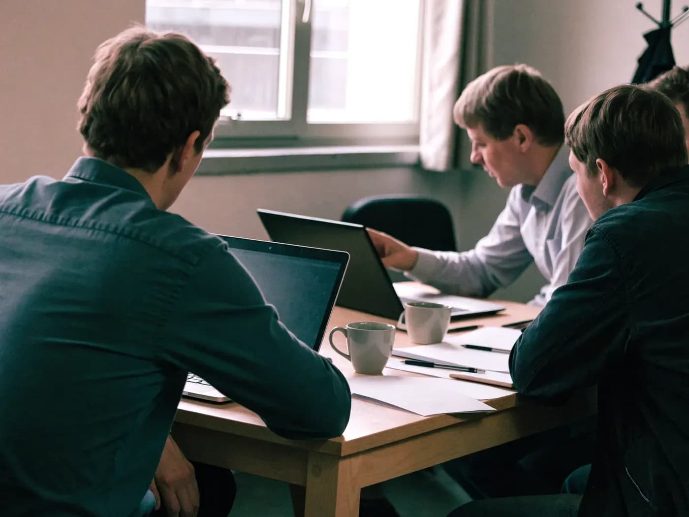 Klein gezelschap ondernemers rond een tafel met laptops, iemand wijst iets aan op een scherm